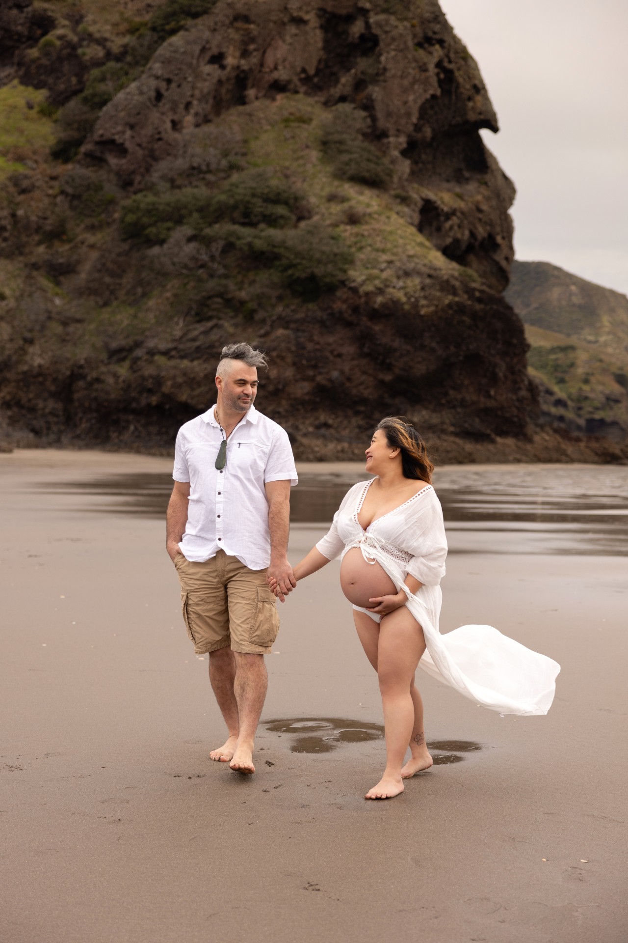 couple walking on the beach with preganant belly