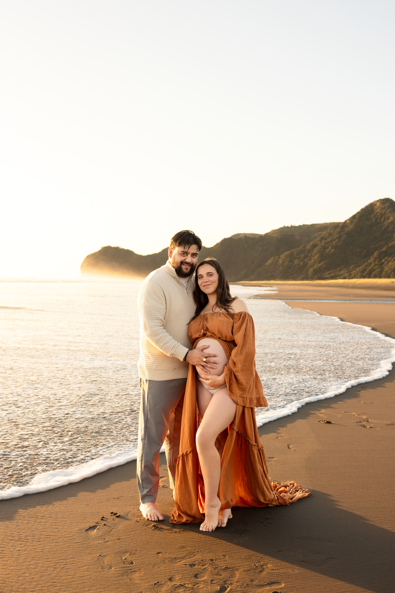 dad holding pregnant belly and ocean is close