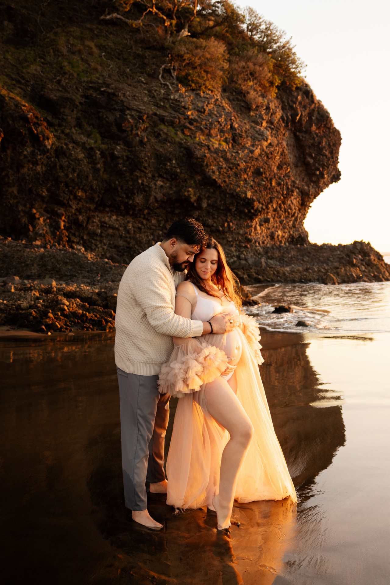 pregnant couple standing at front of the cliff at beach