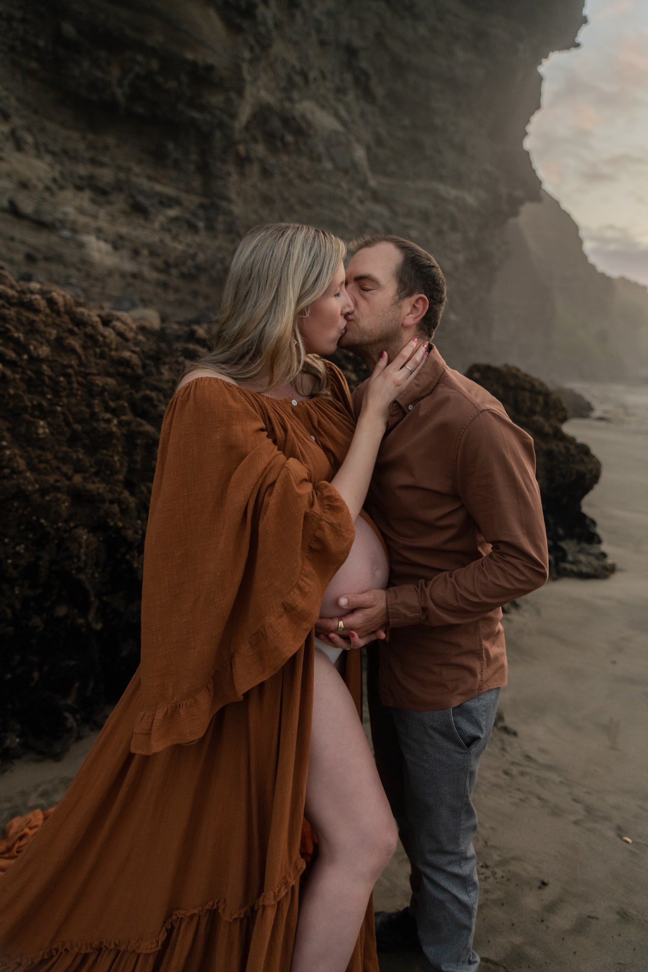 couple is showing a pregnant baby bump while kissing in front of the cliffs