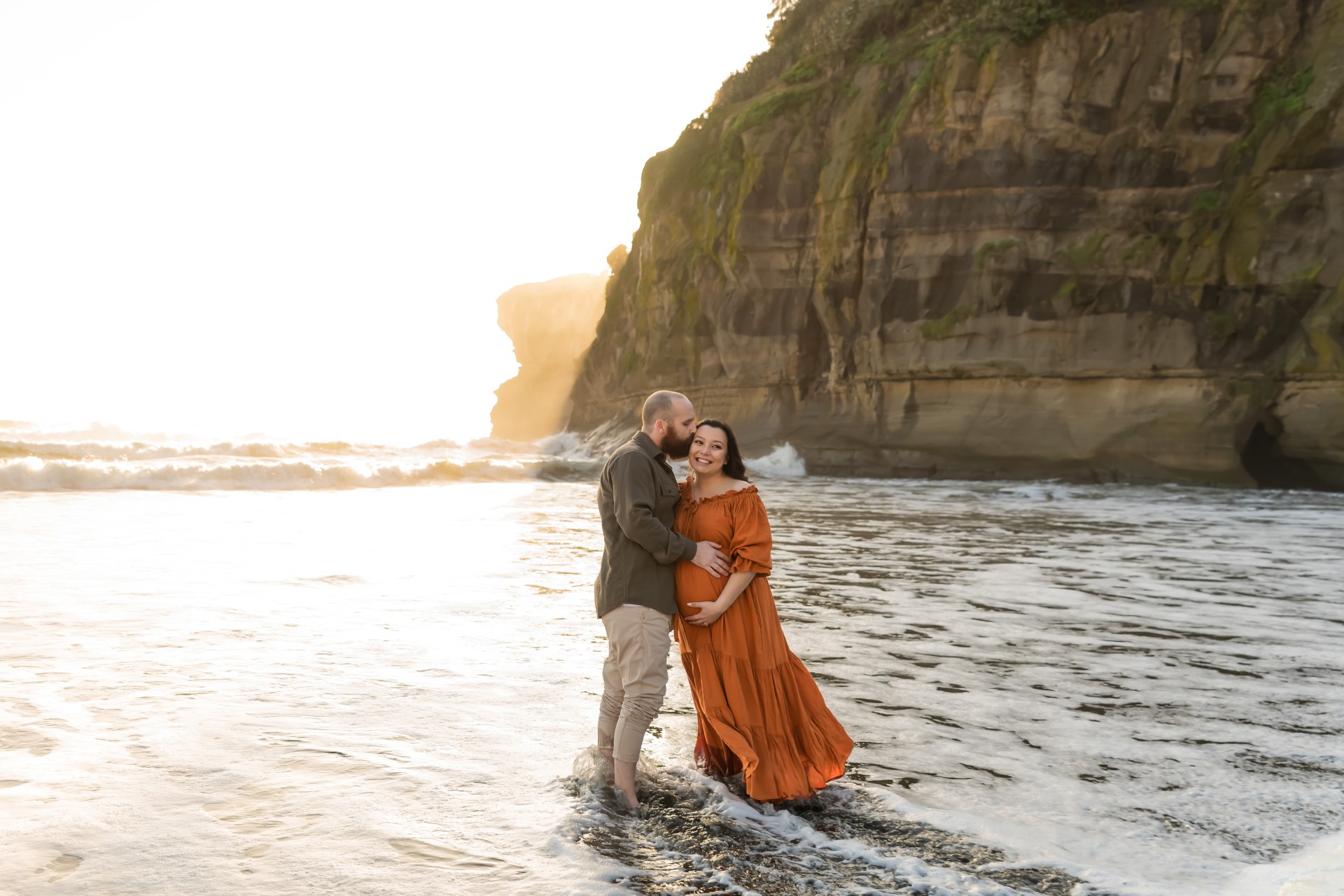 maternity photo of a couple on the murriwai beach surrounded by white ocean foam