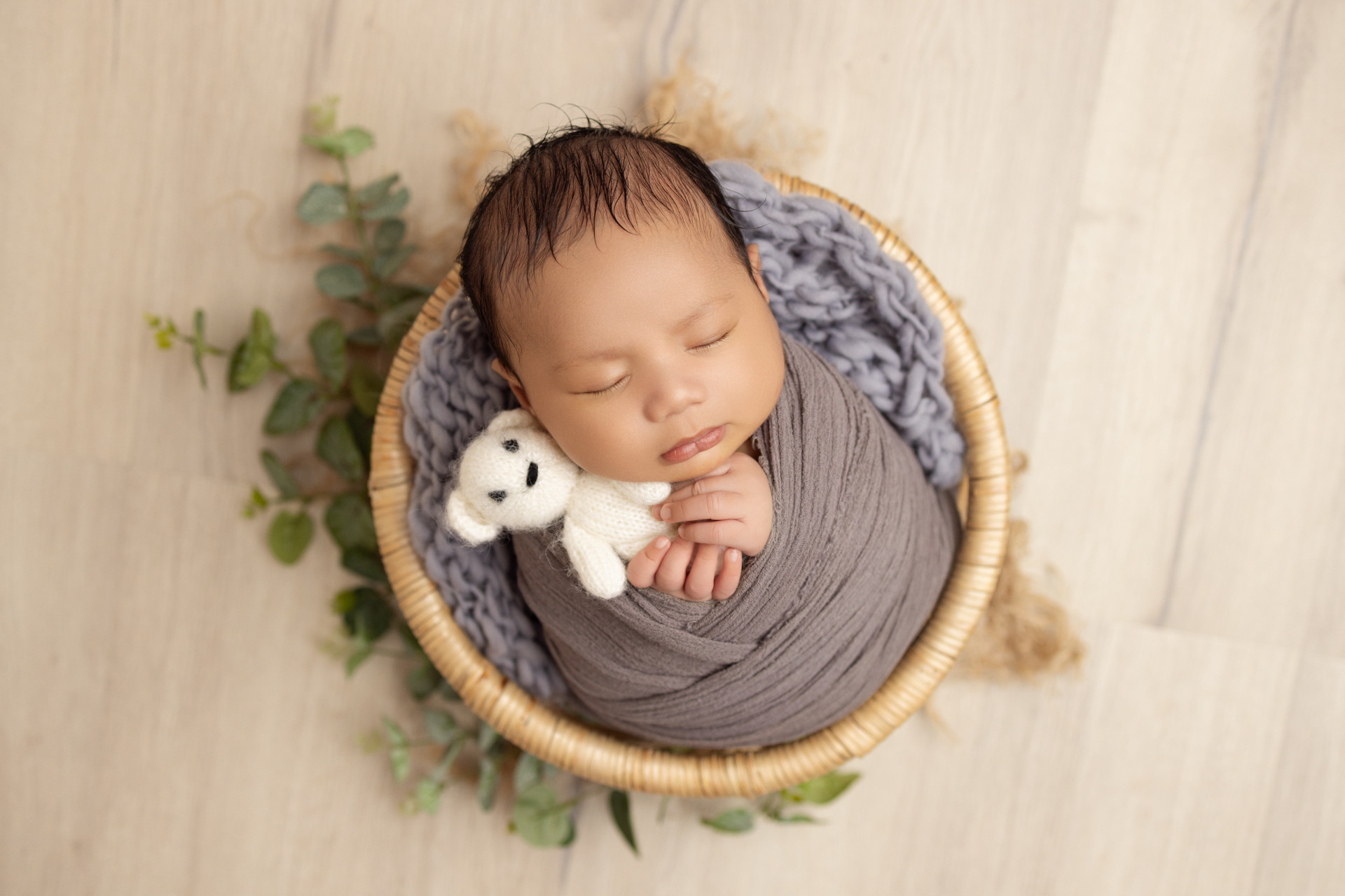baby in round basket holding teddy