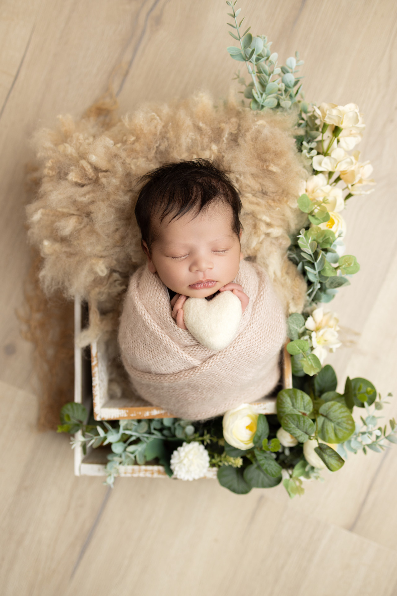 baby surrounded with flowers holding heart