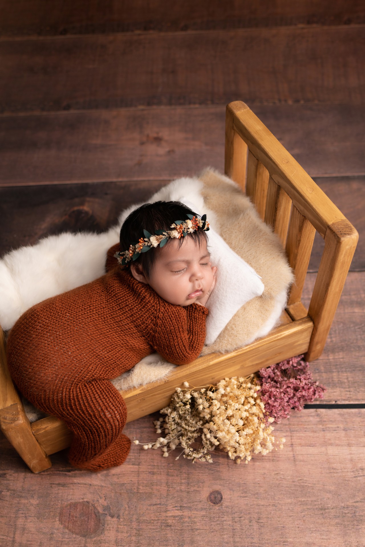 baby sleeping in the baby bed with one leg down and wearing floral crown