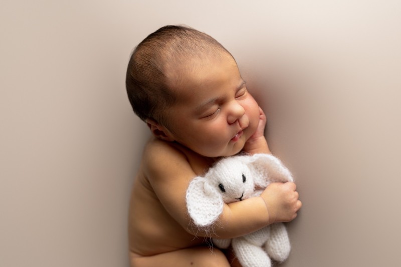 side profile newborn photo, with baby sleeping and cuddling a toy rabbit