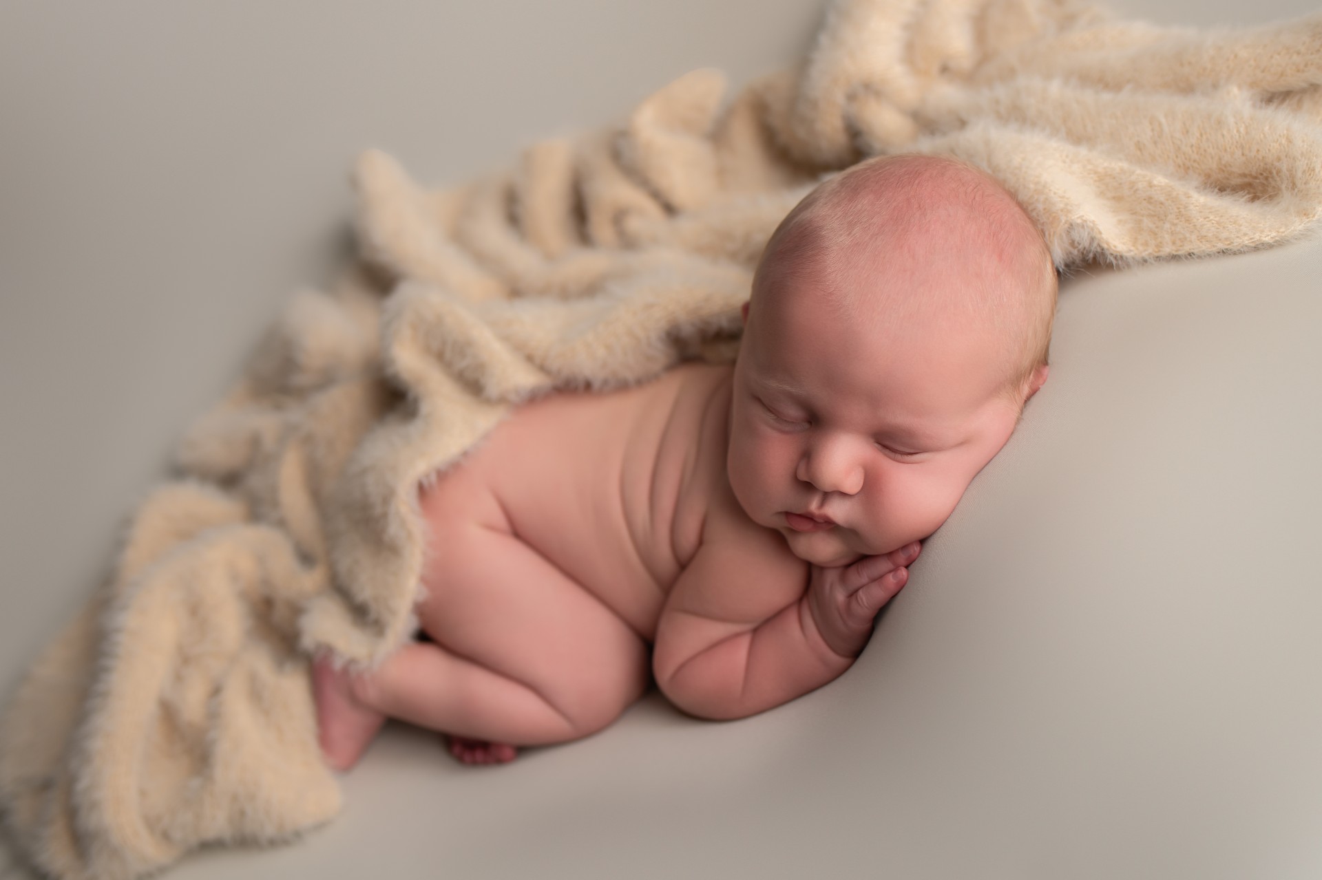 baby sleeping on the tummy covered with beige cashmere wrap