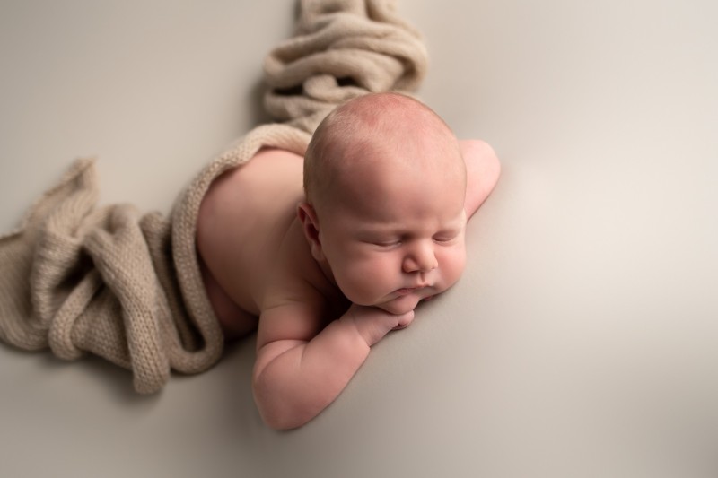 baby sleeping with chin on hands, he is covered with a knitted wrap