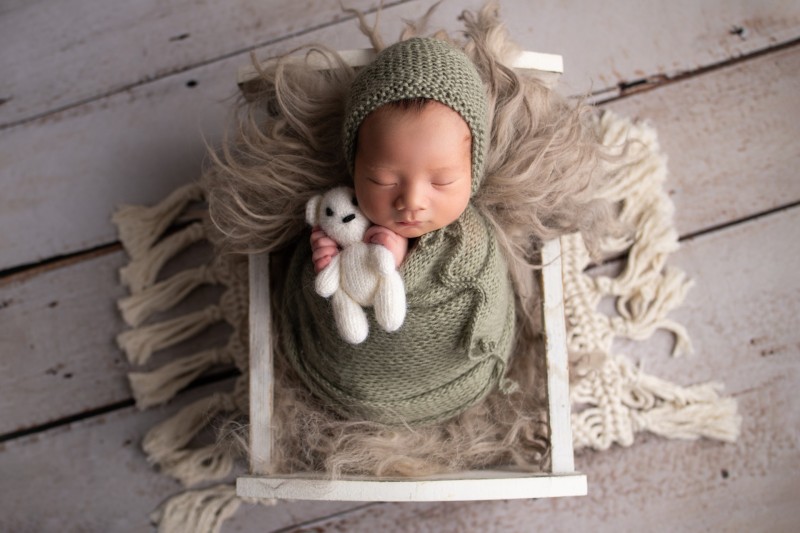 newborn baby wraped in green wrap holding a teddy